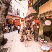A vibrant outdoor market scene displaying hanging brass pots and people shopping, marrakech cultural tours